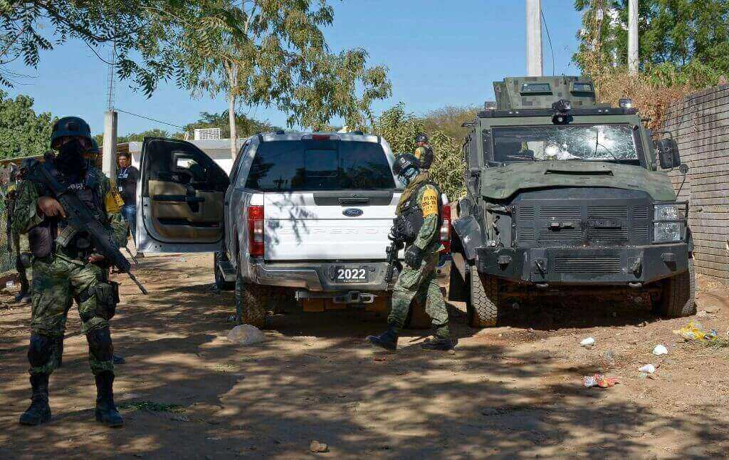 Photograph of soldiers stand guard next to an Army vehicle in Mexico